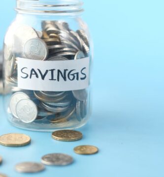 Frasco de vidrio etiquetado como ahorro lleno de monedas junto a una calculadora, para calcular cuánto necesitas en tu fondo de emergencia