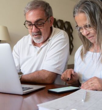 Pareja revisando documentos de su plan personal de retiro con una laptop y una calculadora sobre la mesa