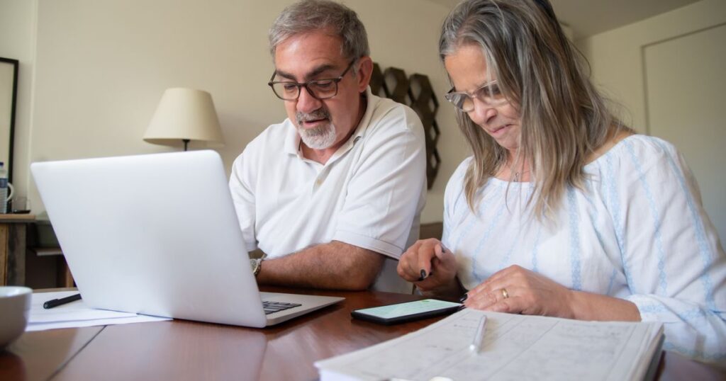 Pareja revisando documentos de su plan personal de retiro con una laptop y una calculadora sobre la mesa