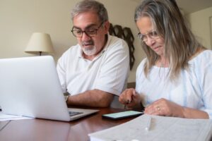 Pareja revisando documentos de su plan personal de retiro con una laptop y una calculadora sobre la mesa