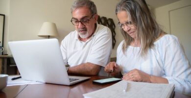 Pareja revisando documentos de su plan personal de retiro con una laptop y una calculadora sobre la mesa