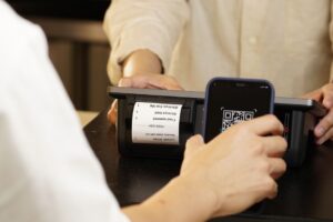 Persona pagando con su teléfono celular mediante un código QR en el mostrador de un comercio, ejemplo de un cobro con CoDi en México