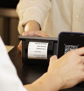 Persona pagando con su teléfono celular mediante un código QR en el mostrador de un comercio, ejemplo de un cobro con CoDi en México