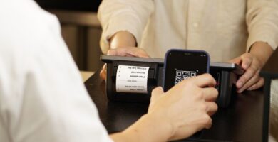 Persona pagando con su teléfono celular mediante un código QR en el mostrador de un comercio, ejemplo de un cobro con CoDi en México