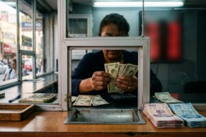 Ventanilla de una casa de cambio con un tablero de precios de compra y venta del dólar y billetes de pesos y dólares sobre el mostrador